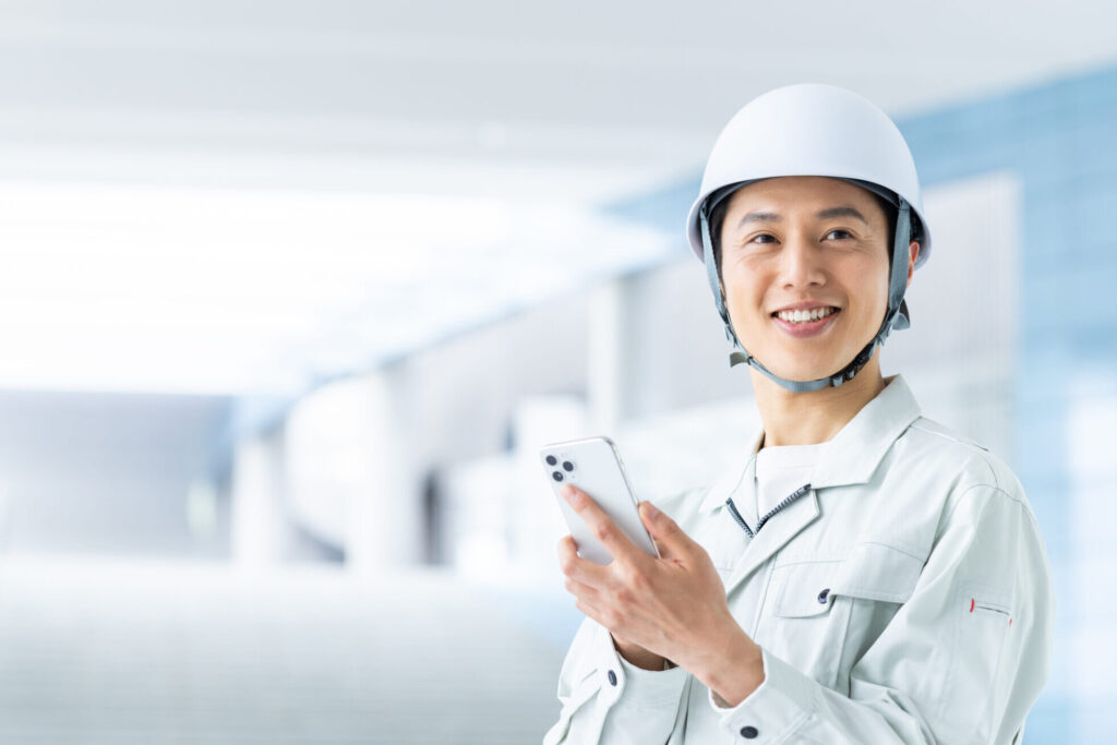 スマホをいじるヘルメットをかぶった作業員